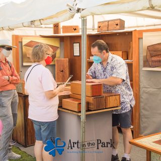 Art in the Park 2021 artist with patrons showing them wooden musical percussion instruments