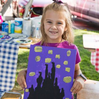 Art in the Park 2021 young girl smiling holding up her starry night like painting